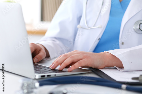 Close up of unknown female doctor typing on laptop computer while sitting  at the table. Medical staff  compulsory work concept
