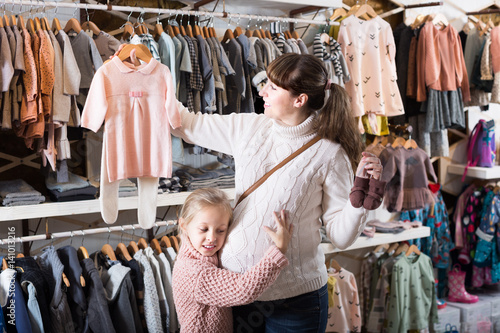 Positive pregnant female and daughter choosing clothes