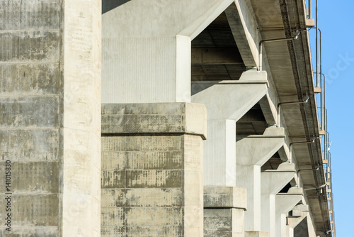 Underside of viaduct with gray concrete pillars, drainpipes and protruding road.