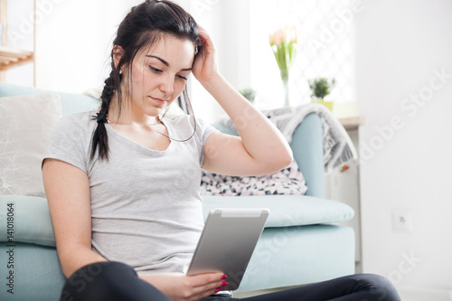 Young woman using pc tablet while sitting near comfortable sofa