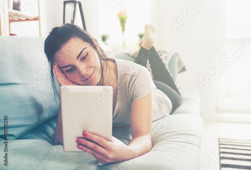 Young woman using pc tablet while lying on comfortable sofa