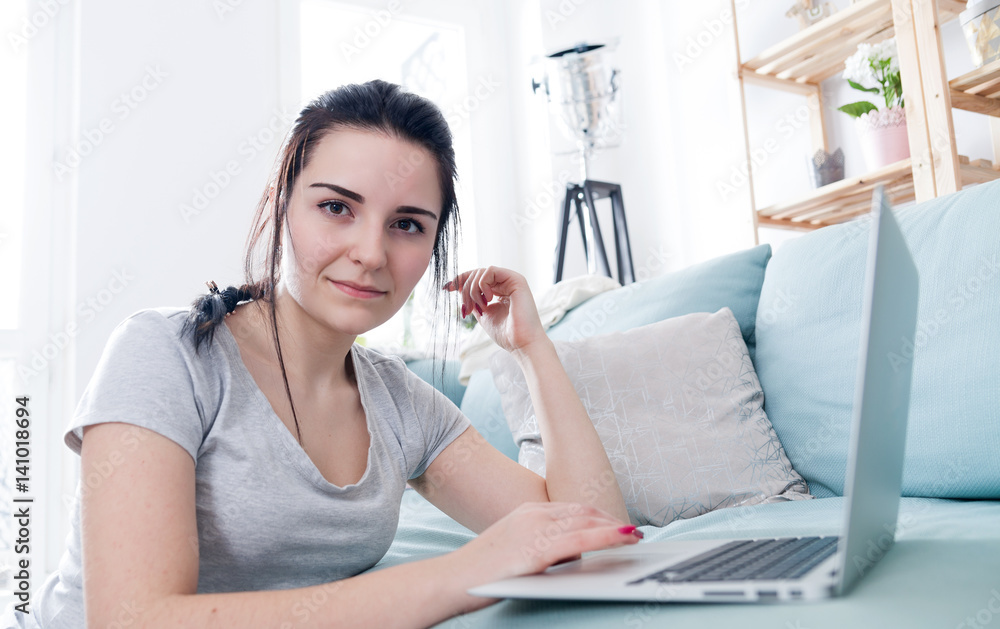 Young woman using laptop while sitting near comfortable sofa, home Young woman using laptop while sitting near comfortable sofa, home