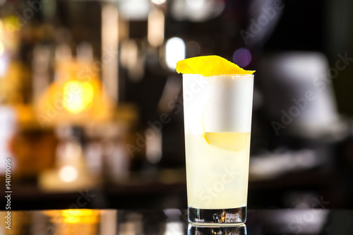 Closeup glass of gin fizz cocktail with lemon and whip eggwhite at bar cpunter background.