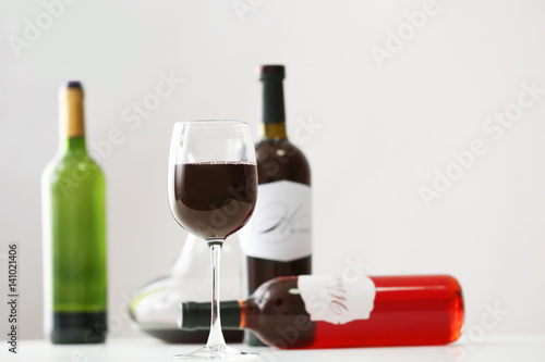 Table with wineglass and bottles of red wine on light background