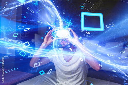 Young man with headset playing virtual reality with blue glowing media stream and particles