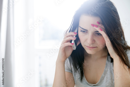 Fotografie Unhappy worried woman talking on phone at home