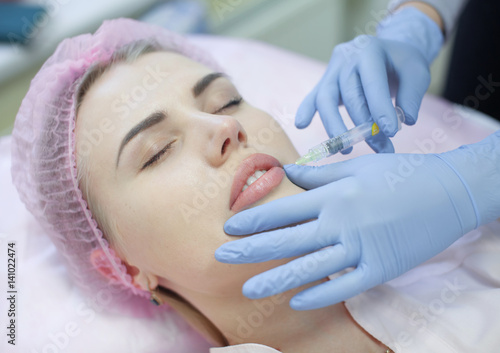 Hands of cosmetologist making injection in face, lips. Young woman gets beauty facial injections in salon. Face aging, rejuvenation and hydration procedures. Aesthetic cosmetology. Close up.