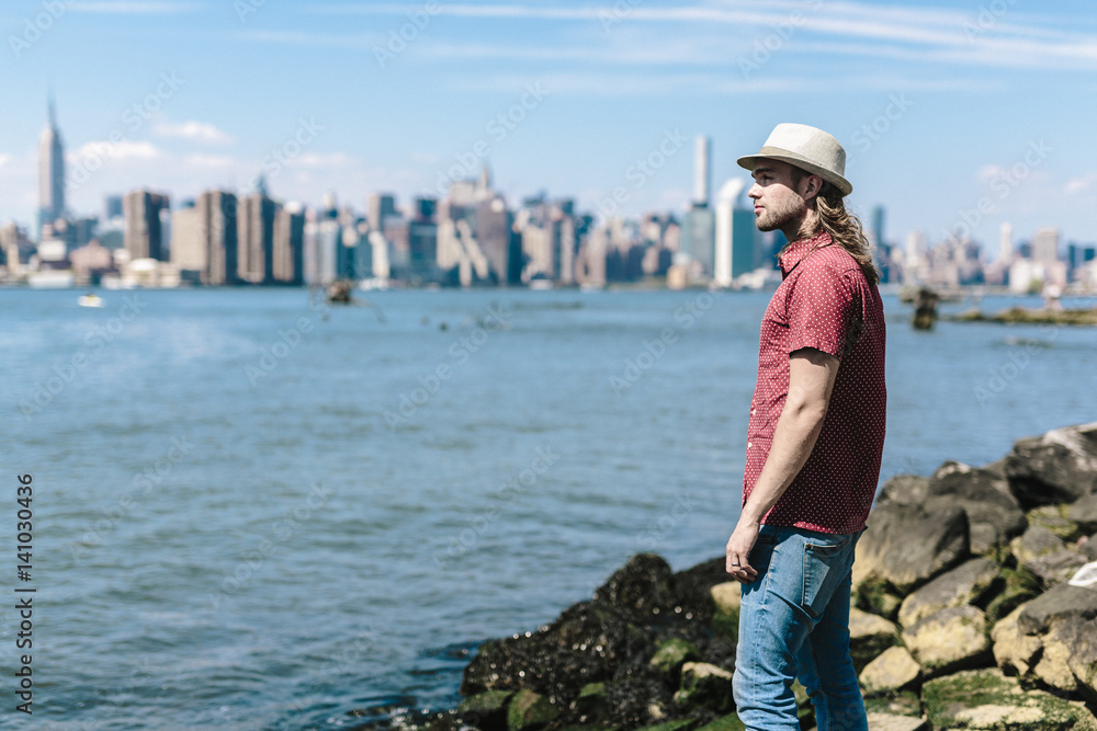 USA, New York City, man wearing hat at the waterfront with Manhattan ...