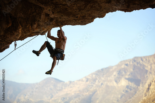 Young man struggling to climb ledge on natural cliff