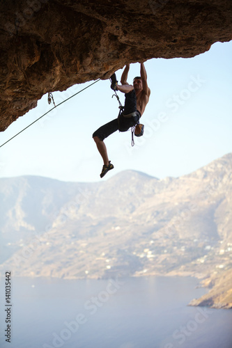 Young man struggling to climb ledge on cliff