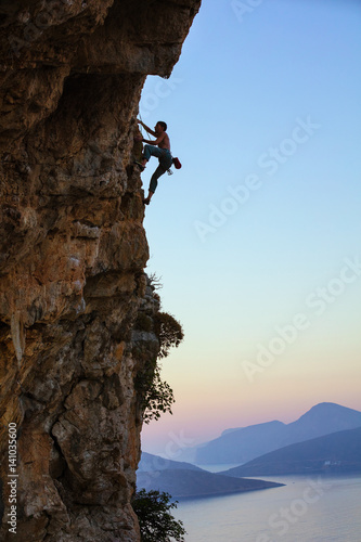 Young man climbing vertical cliff at sunset