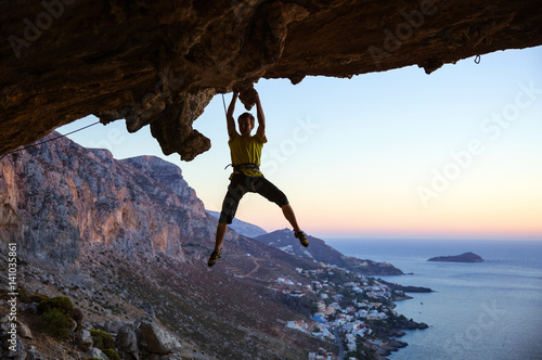 Male rock climber gripping handhold on ceiling in cave