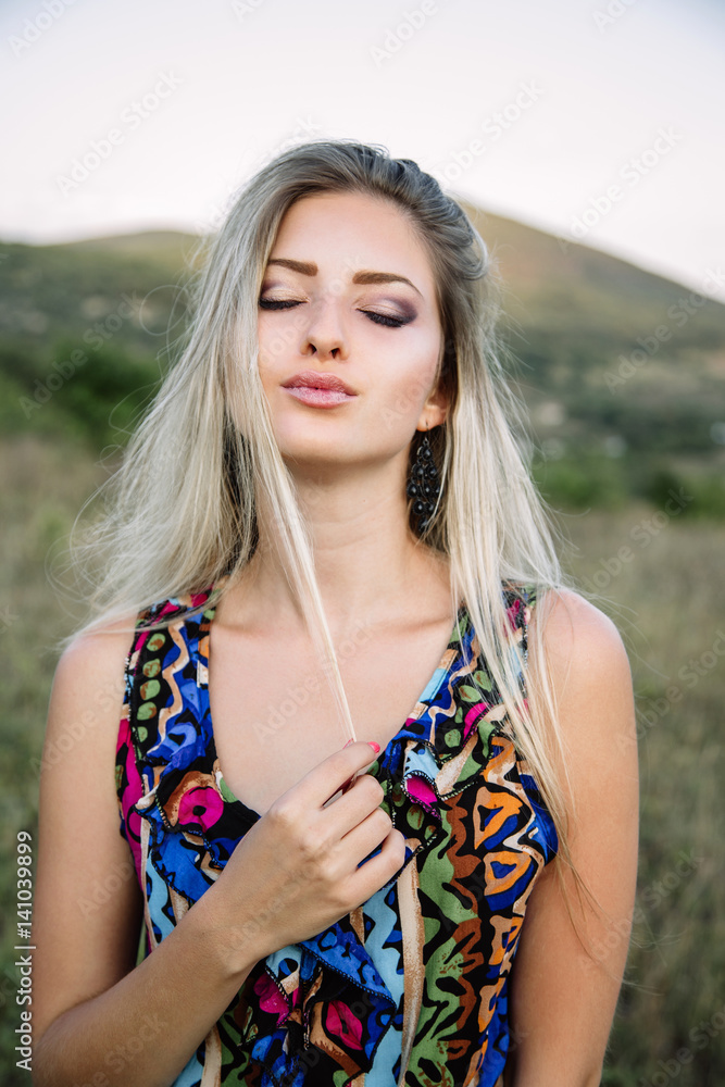 Naklejka premium beautiful dreamy blonde girl with blue eyes in a light turquoise dress lying on the stones