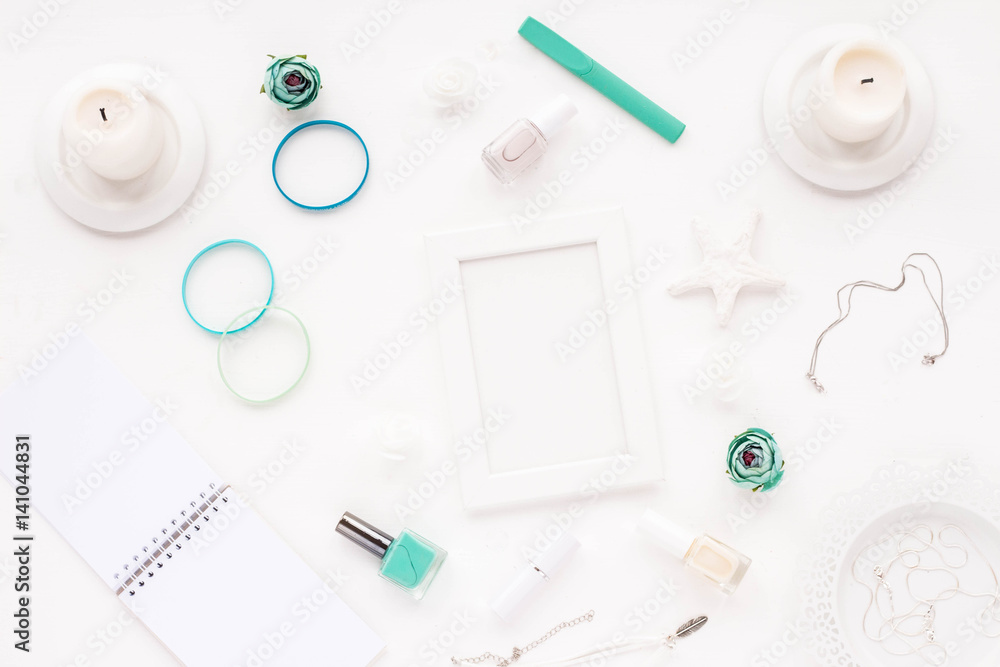 Feminine desk workspace with white frame, notebook, empty blank, stylish woman turquoise accessories, white candles, spring flowers, nail polish on white background. Flat lay, top view. Feminine desk workspace with white frame, notebook, empty blank, stylish woman turquoise accessories, white candles, spring flowers, nail polish on white background. Flat lay, top view.