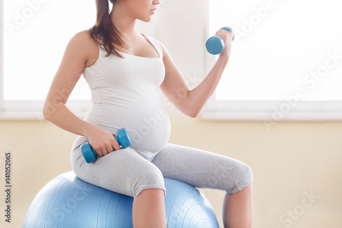 Portrait of a beautiful young pregnant woman executing exercises with fitball