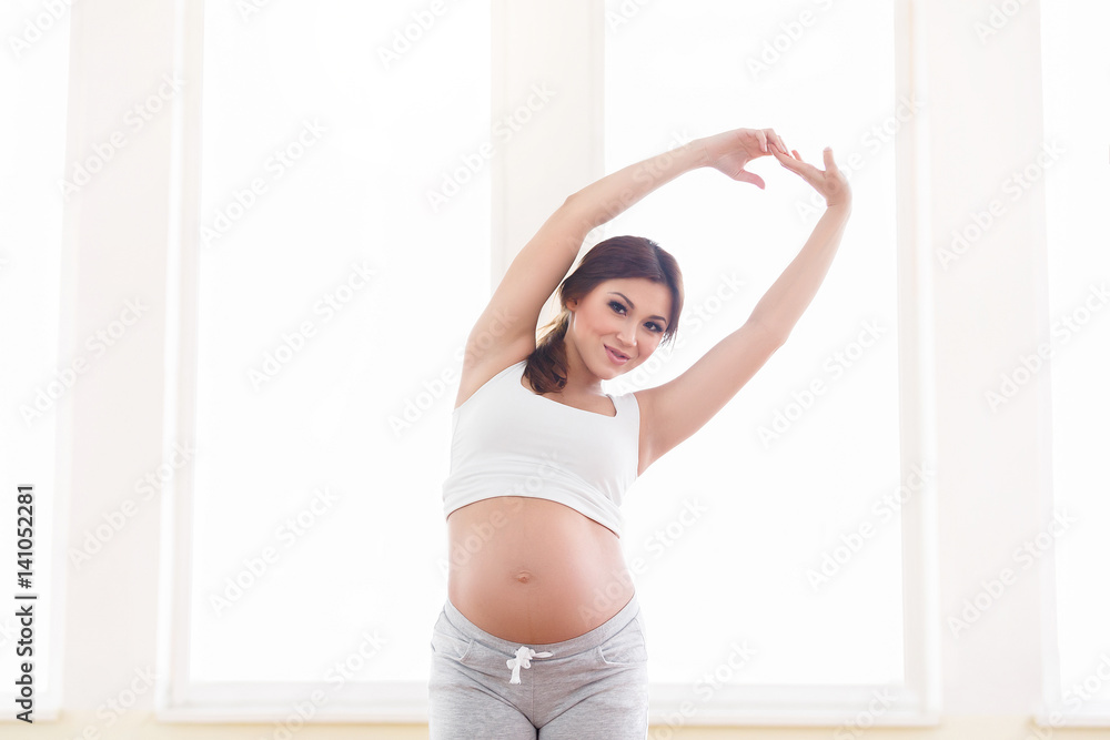 Young beautiful pregnant woman standing near window at home Young beautiful pregnant woman standing near window at home
