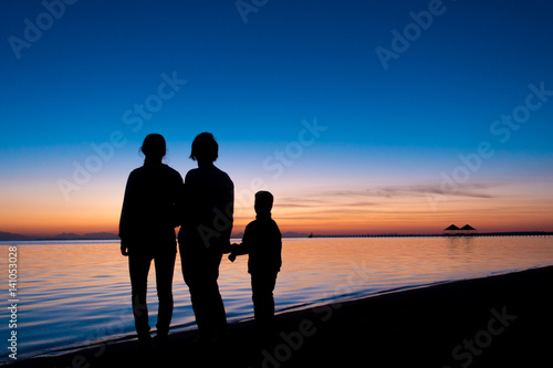 silhouette of three people standing on the beach in sunrise © Sergiy Bykhunenko