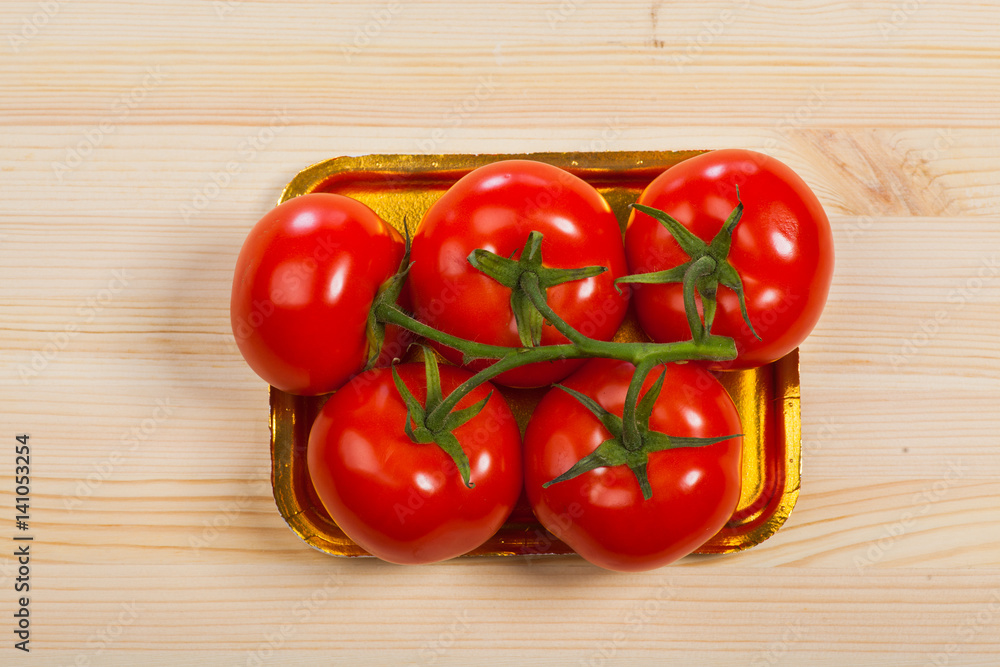 Five fresh red tomatoes with green stem in the tray , isolated on the background Five fresh red tomatoes with green stem in the tray , isolated on the background