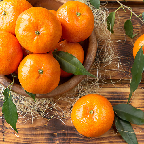 Fresh juicy tangerine fruits close-up in a wooden plate on a wooden background with leaves in a rural rustic style top view