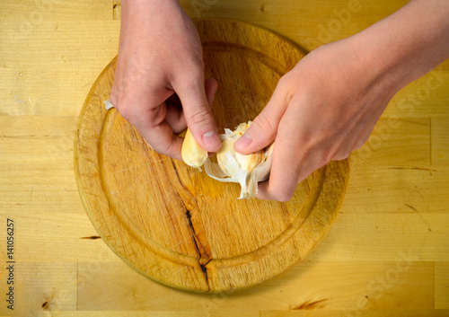 cooking and home concept - close up of male hands taking off peel of garlic on cutting board