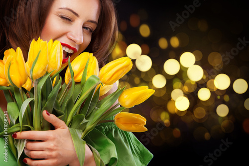Closeup girl portrait. Beautiful brunette woman smiling with tulip flowers in hands on black background with bokeh lights.