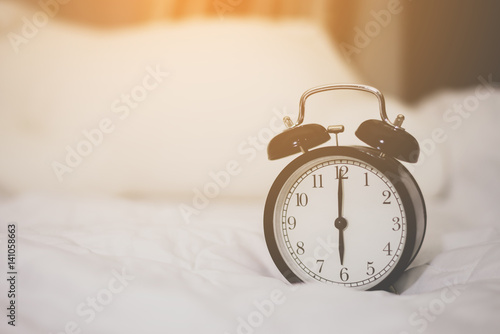 Black Alarm Clock on White Bed Background with Sunlight from the Window in Morning Time