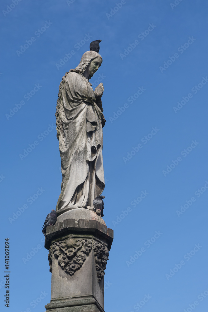Maria sculpture of stone with a dove on the head, Mary's column from Kaspar von Zumbusch 1861 in Paderborn, blue sky with copy space