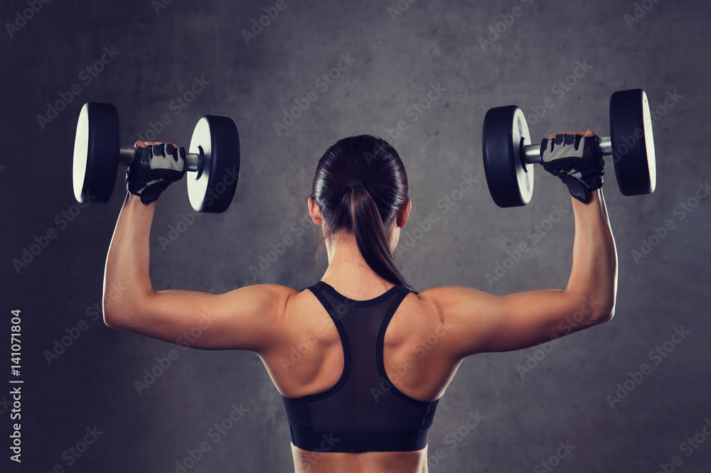 Obraz premium young woman flexing muscles with dumbbells in gym