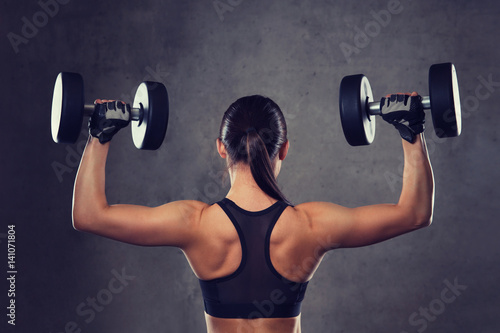 young woman flexing muscles with dumbbells in gym