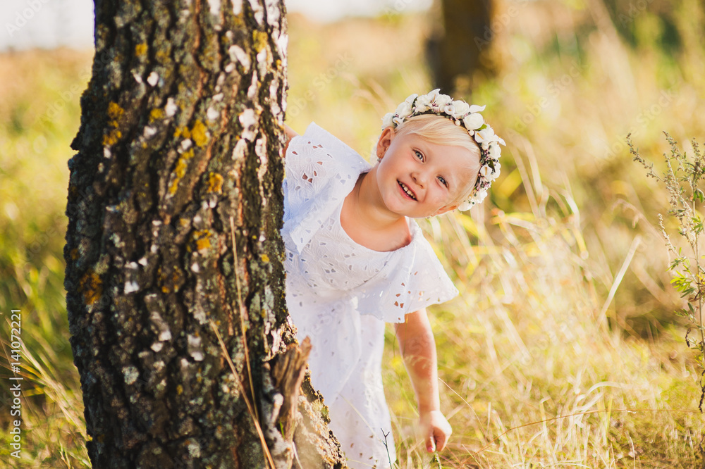 little girl standing behind a tree in the park outdoors, playing hide and seek, a beautiful white dress little girl standing behind a tree in the park outdoors, playing hide and seek, a beautiful white dress