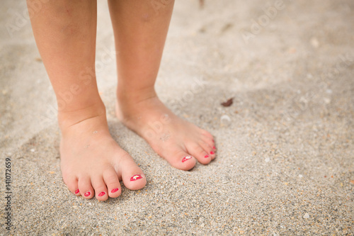 Closeup of a little girl's legs and feet walking on the sand of the beach with the sea water in the background summer © goodmoments
