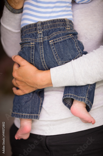 Fototapeta Naklejka Na Ścianę i Meble -  Closeup of woman's hands holding baby in blue jeans. Mother hugging her son. Together. Family.