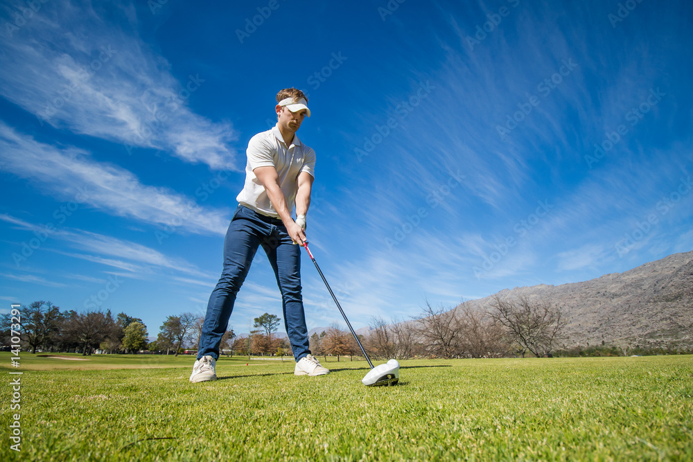Wide angle view of a golfer teeing off from a golf tee on a bright sunny day on a golf course in south africa. Wide angle view of a golfer teeing off from a golf tee on a bright sunny day on a golf course in south africa.