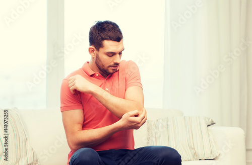 unhappy man suffering from pain in hand at home