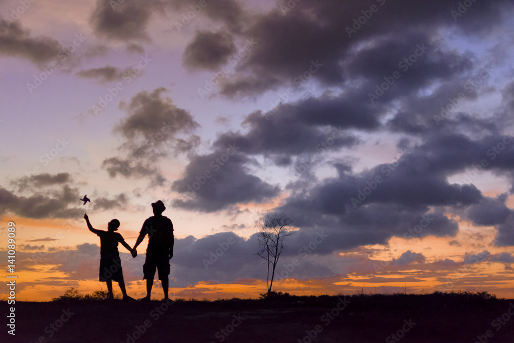 Brother with his brother holding a windmill and background of clouds and sunset .Silhouette concept.