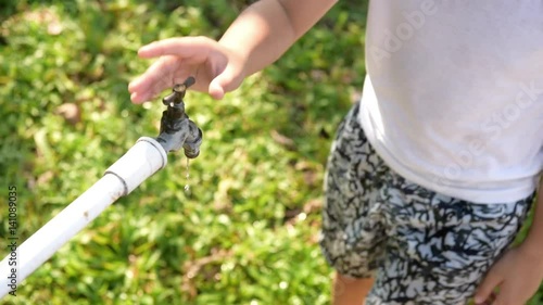 Close up young asian boy taking water from old faucet in the garden. Water shortage and drought concept