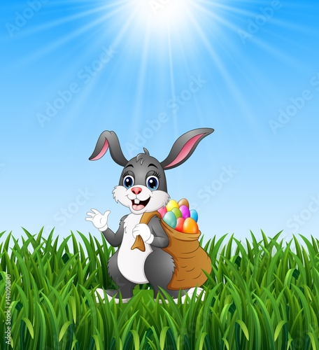 Easter bunny rabbit with easter eggs a sack of full in the grass background 