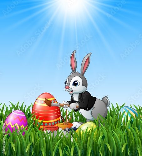 Easter bunny painting easter eggs in the grass background 