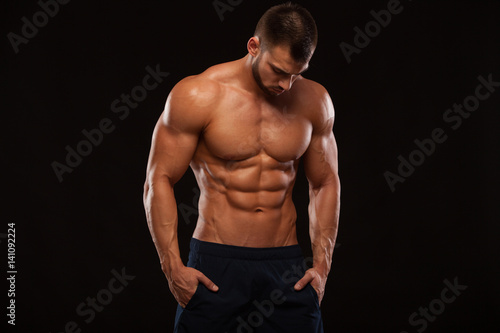 Strong Athletic Man - Fitness Model showing Torso with six pack abs. stands straight and puts his hands in trousers. isolated on black background with copyspace © satyrenko