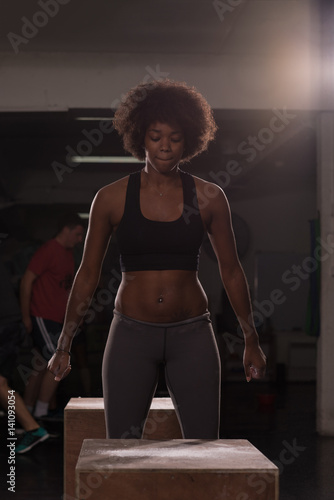 black female athlete is performing box jumps at gym
