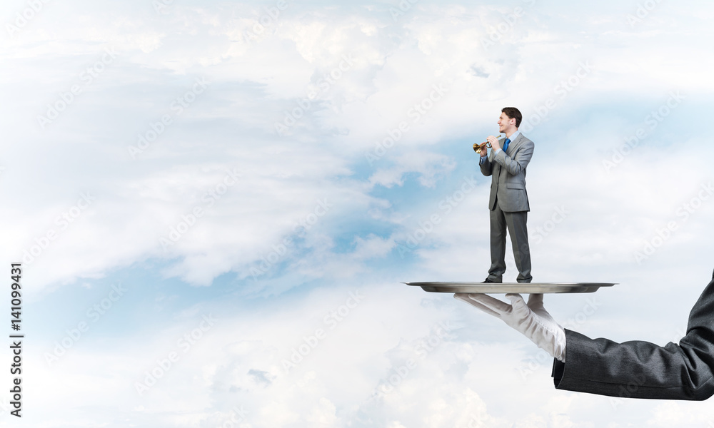 Businessman on metal tray playing fife against blue sky background Businessman on metal tray playing fife against blue sky background