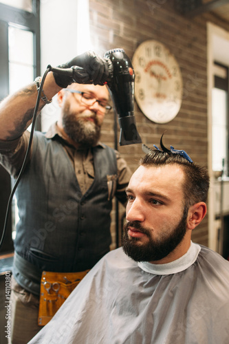 Stylish barber drying mans hair in barbershop. Young man making hairstyle. Beauty, style, modern lifestyle concept