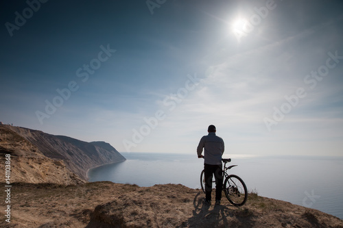 A cyclist stands on the high seashore
