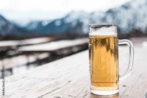 Glass beer on wooden table with mountains background 