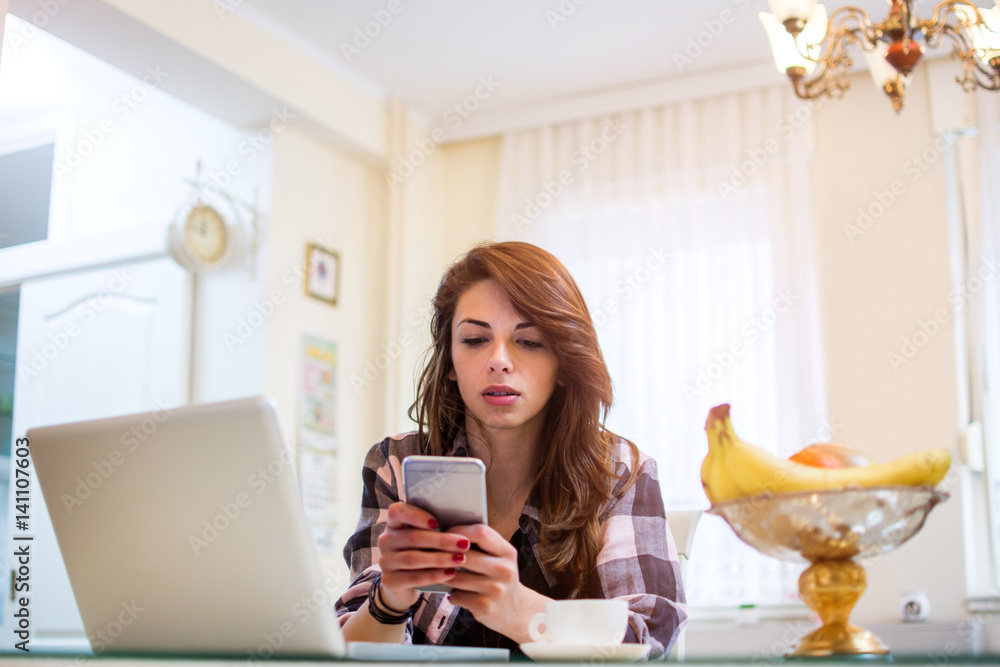 Young woman using phone while having morning coffee at home. Young woman using phone while having morning coffee at home.