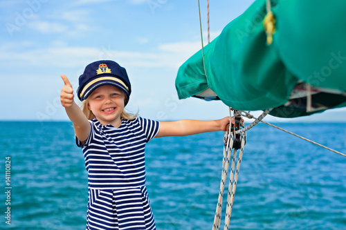 Fotografie Happy little baby captain on board of sailing yacht watching offshore sea on summer cruise