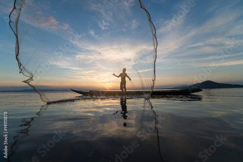 Silhouette of Myanmar fisherman on wooden boat in action catching freshwater fish in nature river at sunset time