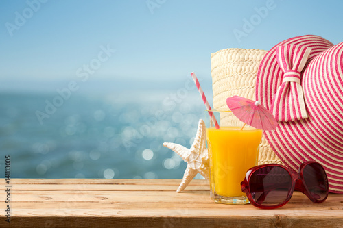 Summer holiday vacation concept with orange juice, hat and sunglasses over sea beach background