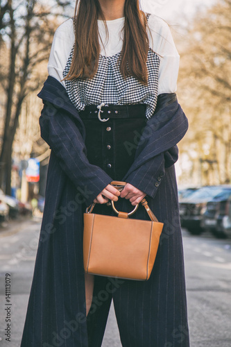 fashion blogger outfit details. fashionable woman wearing a blue oversized coat,checkered shirt, black skirt and a brown trendy handbag. detail of a perfect spring fashion outfit.