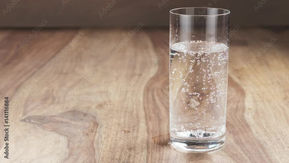 Slow motion of mineral water in glass with air bubbles on wood table, 180fps prores footage Slow motion of mineral water in glass with air bubbles on wood table, 180fps prores footage